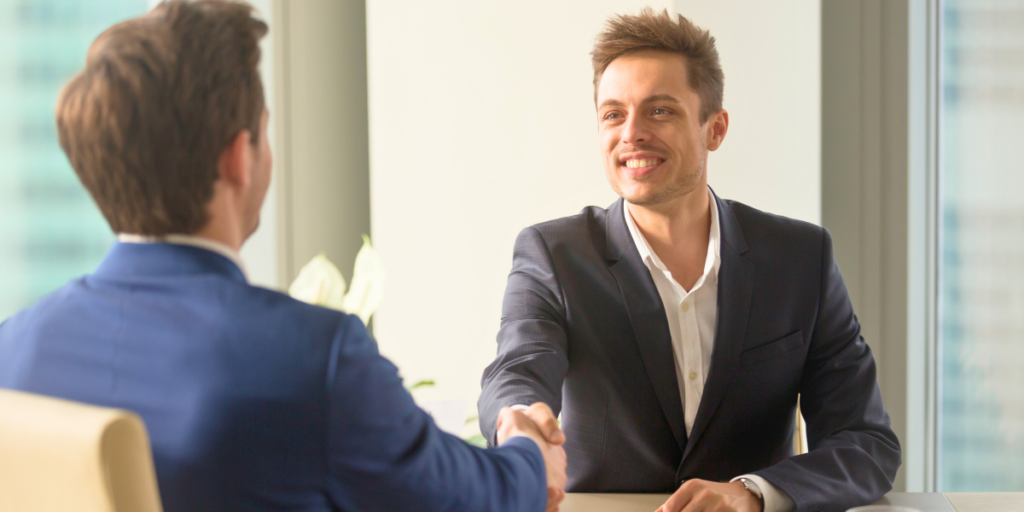 مرشح لوظيفة يبتسم بثقة ويصافح مسؤول التوظيف (HR) في بداية مقابلة عمل ناجحة داخل مكتب حديث.